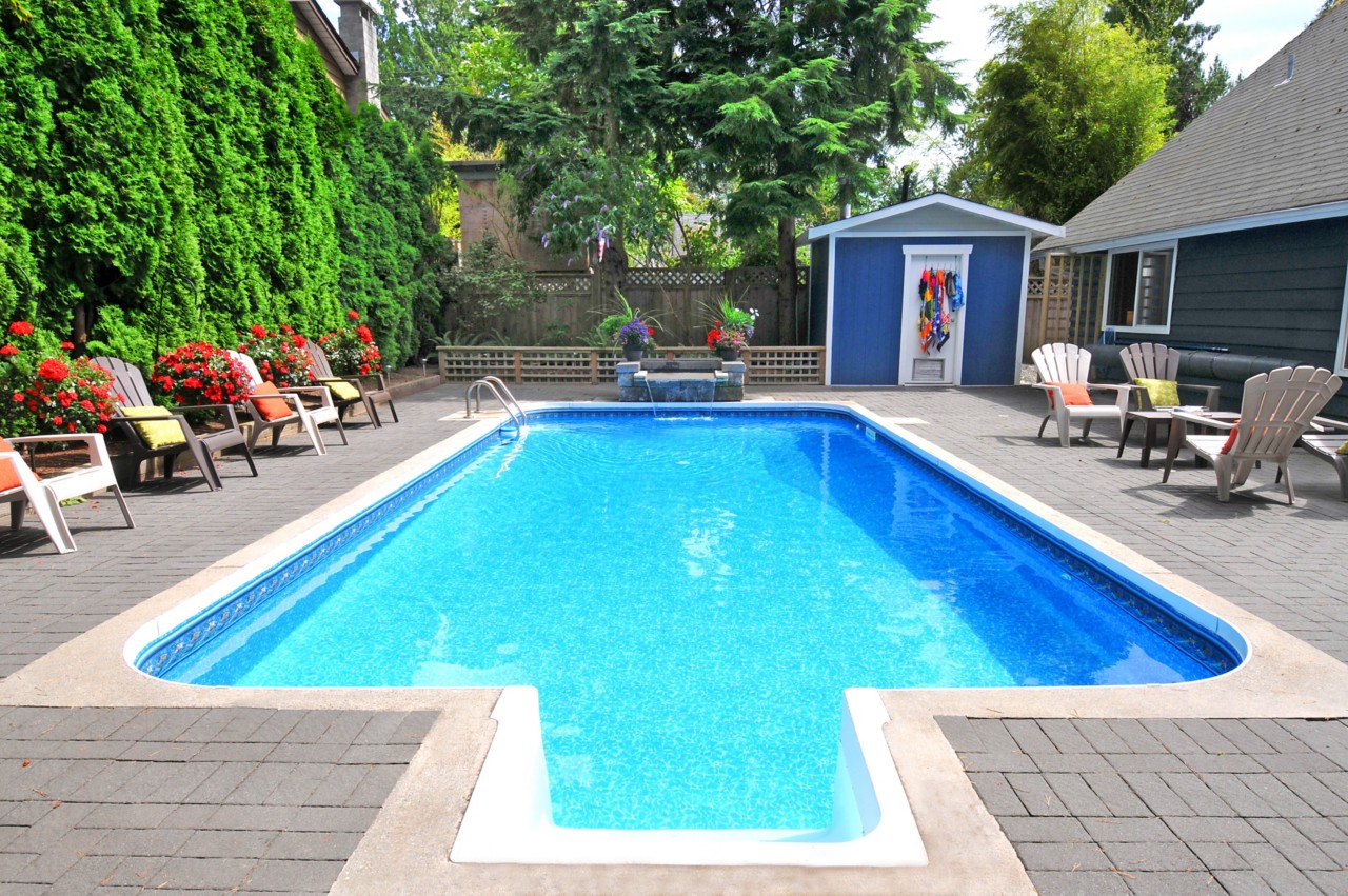 封闭的后院游泳池与瀑布和蓝色泳池房子绿树和阿迪朗达克椅
